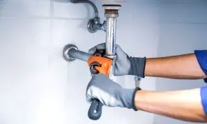 Hydraulik w rękawiczkach dokręca kluczem instalację pod zlewem.